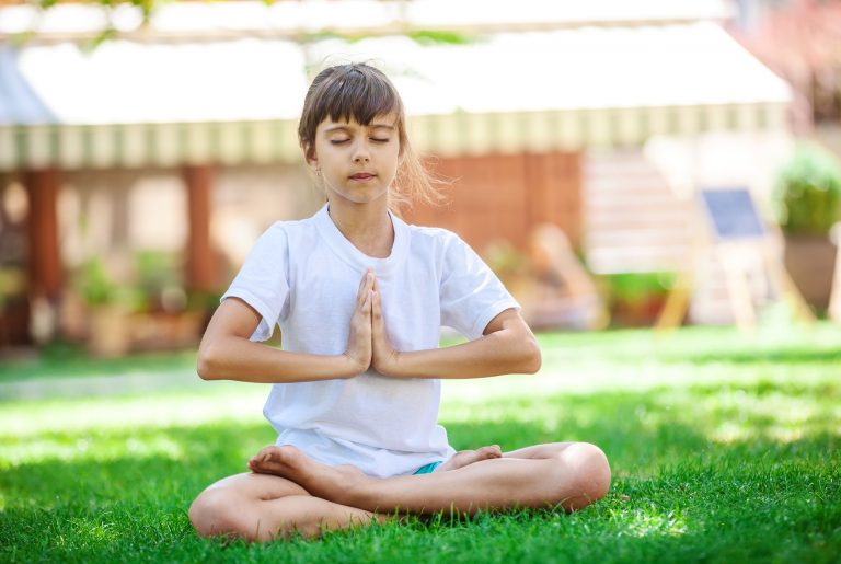 Little girl meditating while sitting in lotus position on grass